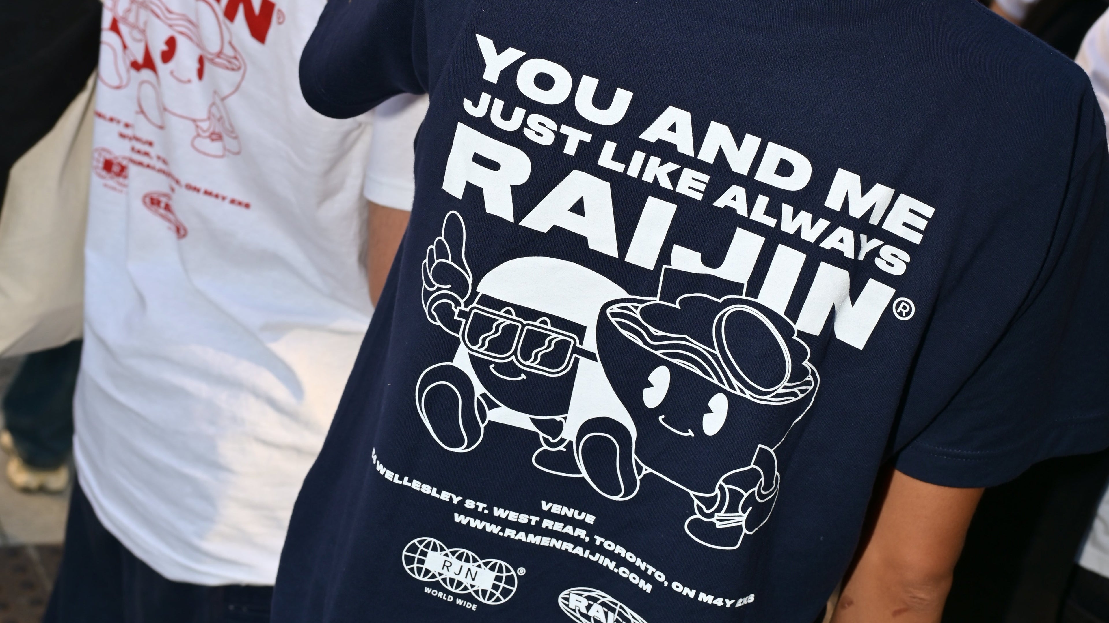 Person wearing a navy blue t-shirt with white text and graphics, standing in front of a white t-shirt with red text and graphics.